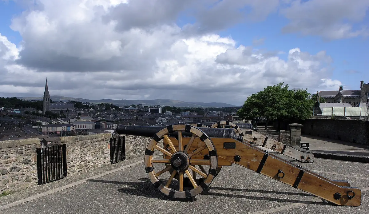 Un cannone storico sulle mura di Derry, con i tetti della città e le colline sullo sfondo