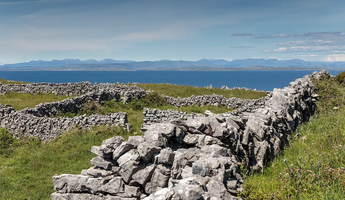 Muretti a secco di pietra calcarea tra prati verdi a Inishmore, con la baia blu all'orizzonte