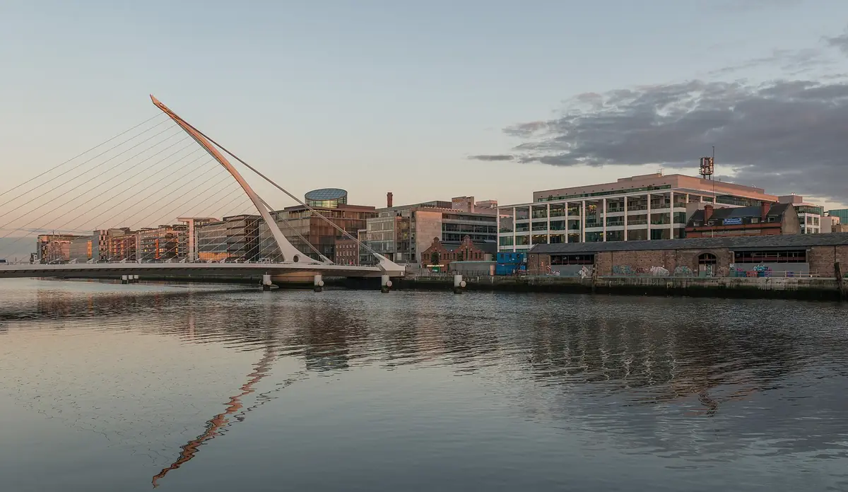 Il Samuel Beckett Bridge a forma di arpa sul Liffey al tramonto, con i Docklands di Dublino riflessi nell'acqua